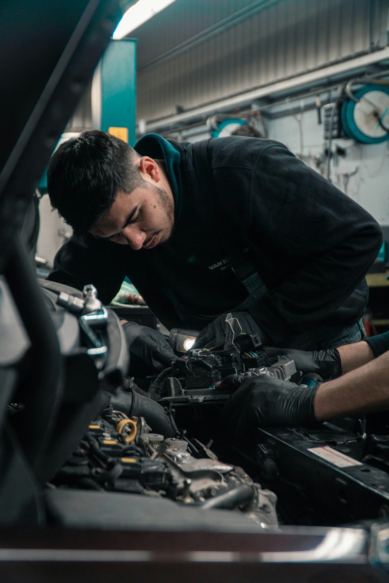 A mechanic in dark overalls working inside an engine bay