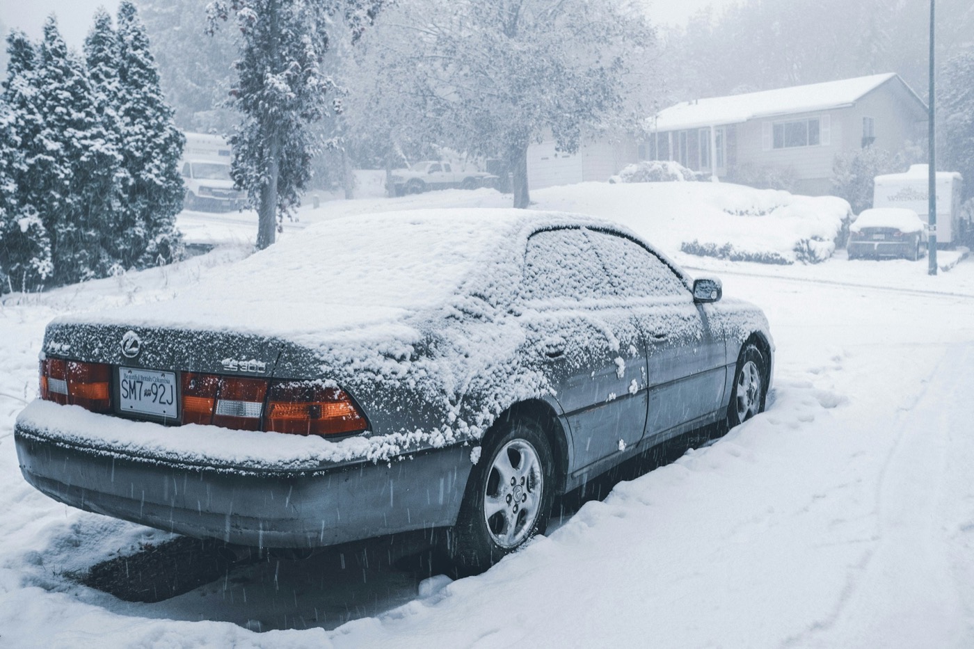 A sedan covered in snow outside a house