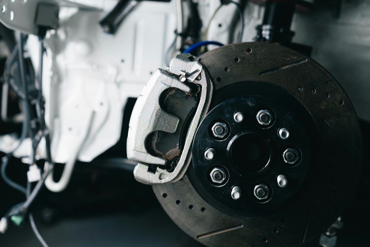 A drilled brake disc and caliper behind a removed wheel