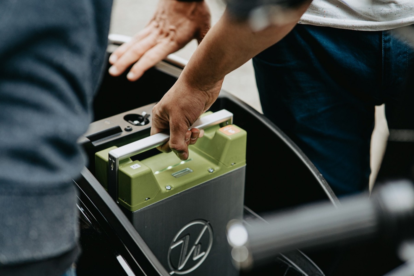 Hands reaching toward a car battery in an engine bay