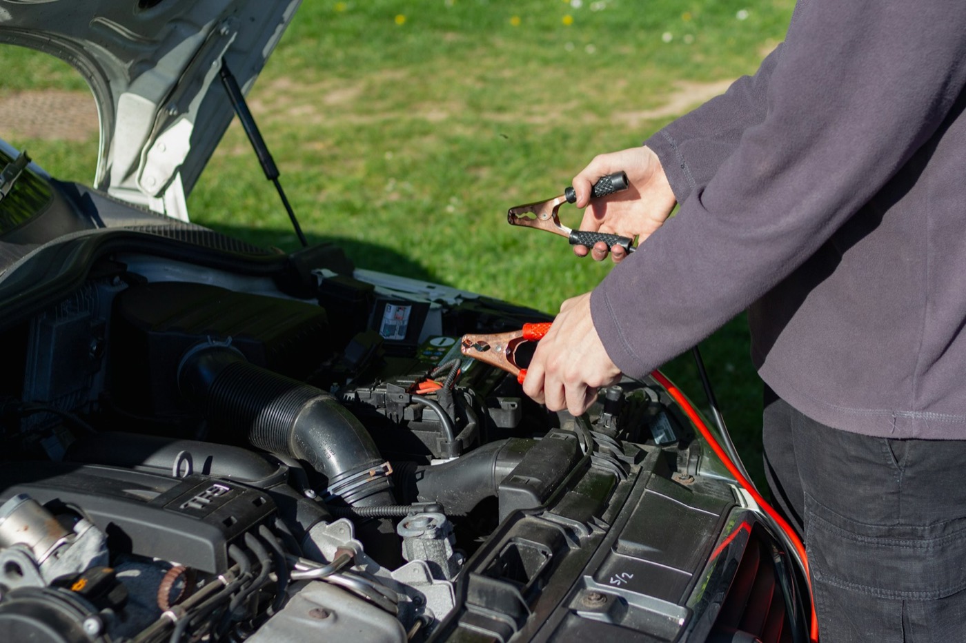 A man connecting jumper cables under the hood of a car