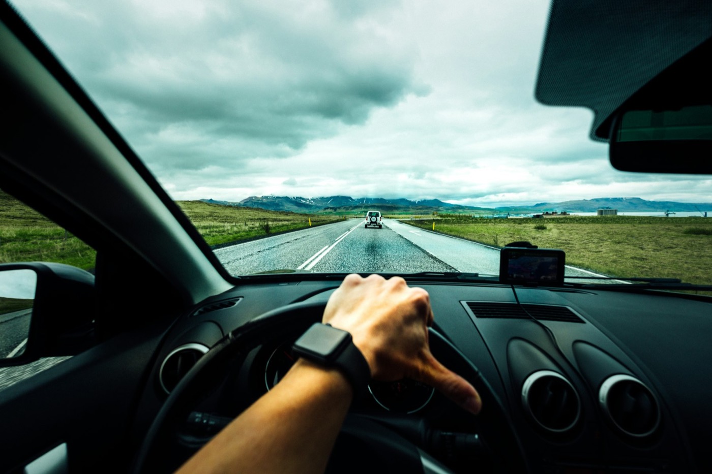 A driver&rsquo;s hand on the steering wheel on an open road